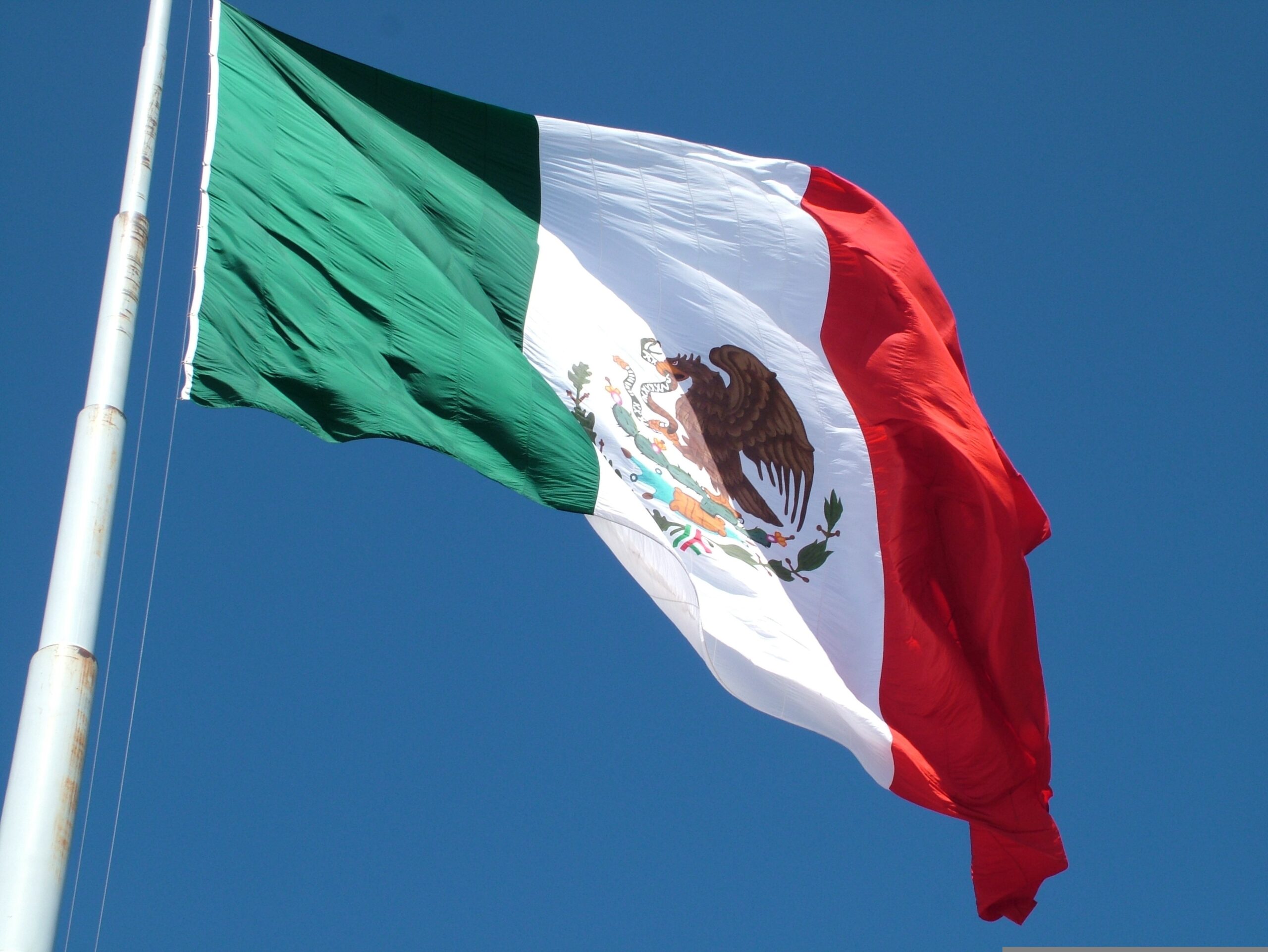 Mexican flag waving under a clear blue sky, symbolizing the vibrant culture and rich history of Mexico.